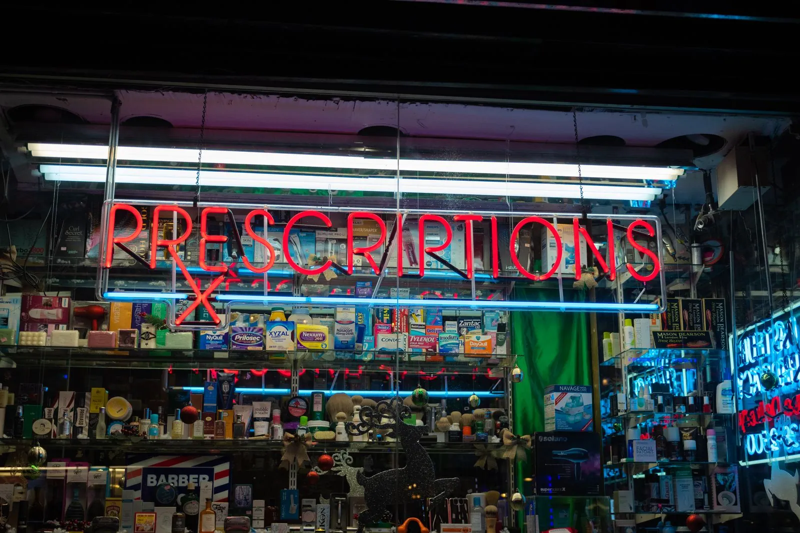 A pharmacy storefront at night lit by a red neon prescriptions sign.