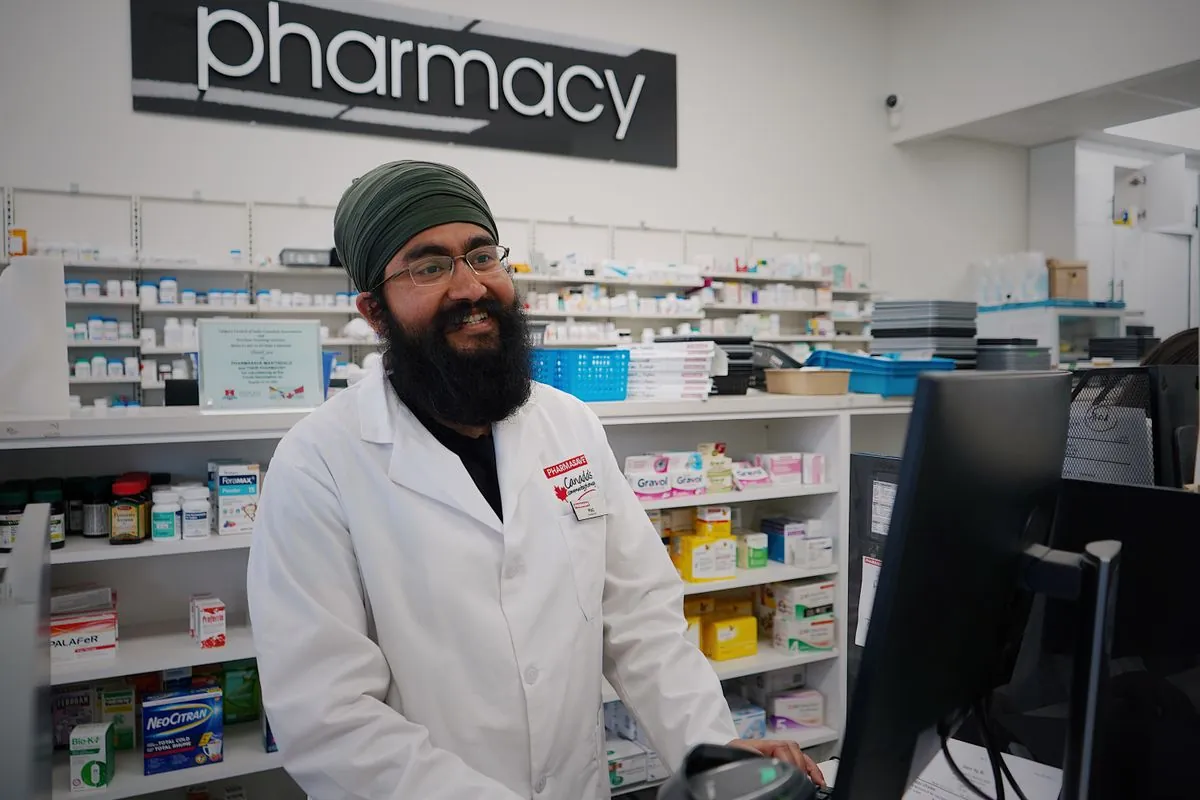 A pharmacist standing behind a pharmacy counter in front of shelves of medicine.