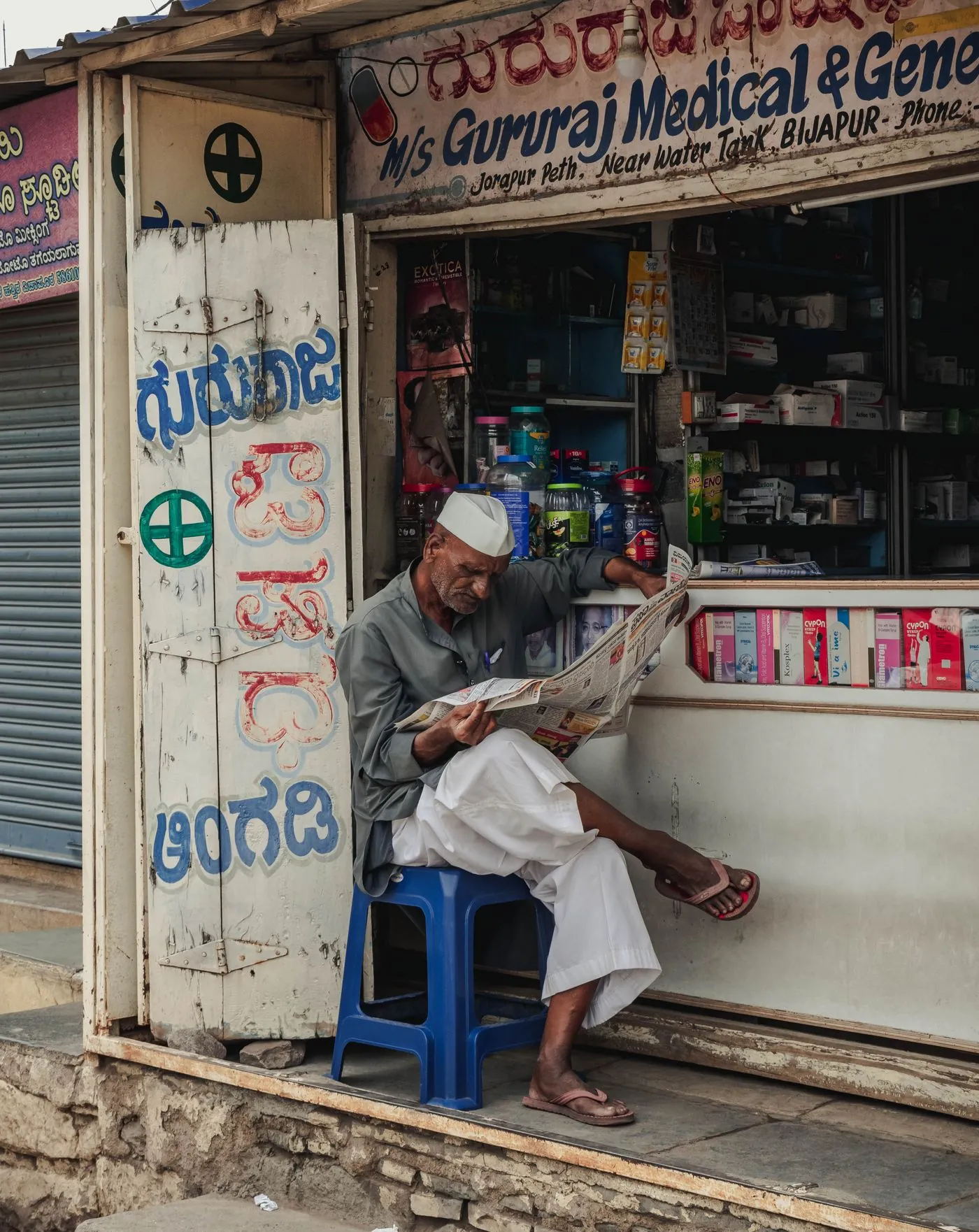 A small medical store on an Indian street, shutters open, a man seated outside.
