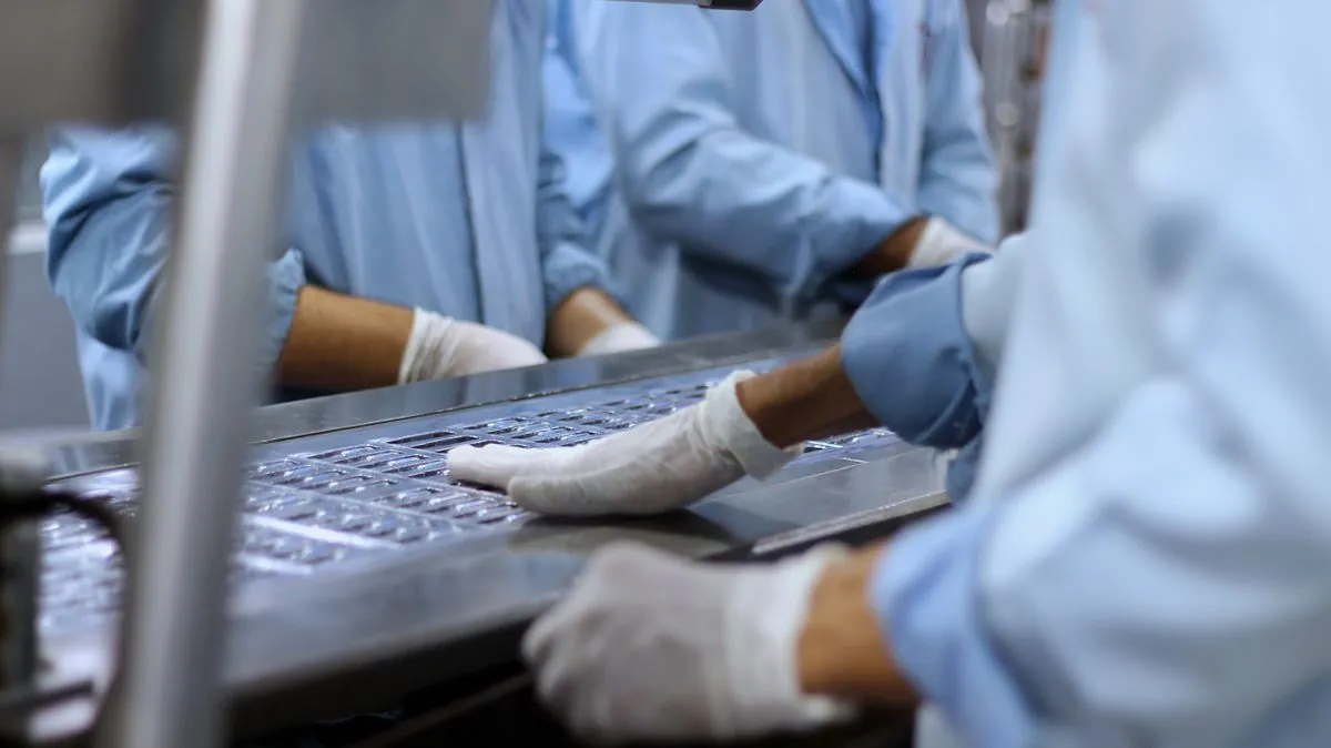 Workers in protective clothing packaging tablets on a production line.