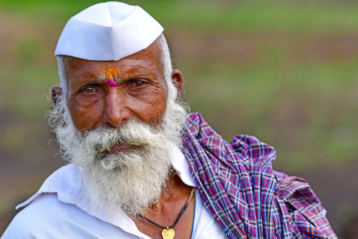 Portrait of an older man with a white beard and cap in rural India.