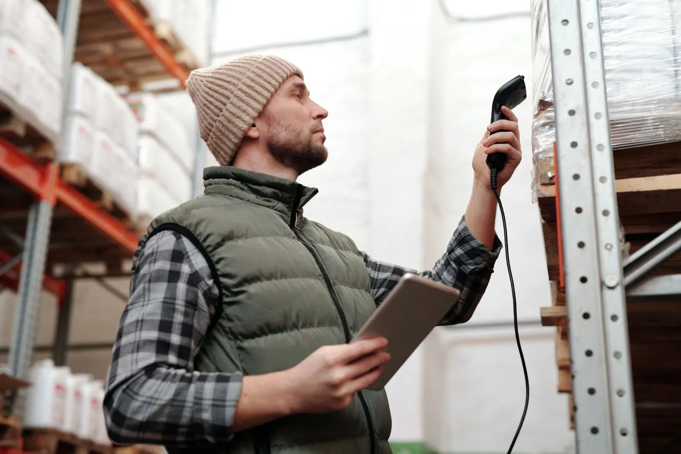 A worker holding a tablet and a handheld scanner beside warehouse racking.